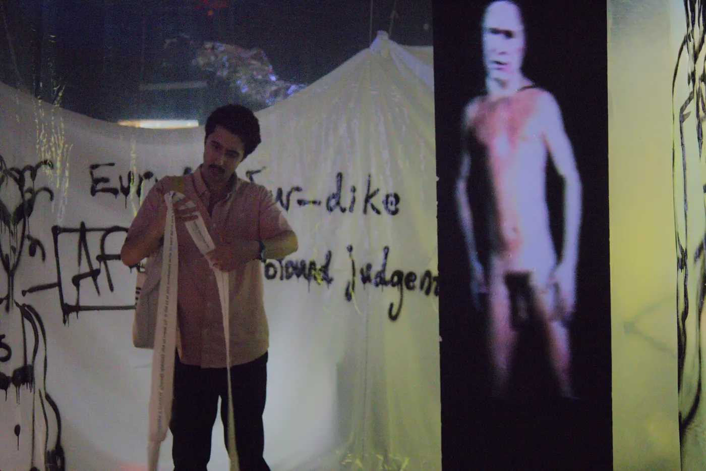 A figure with a shrouded object beside projected text inside the video installation.