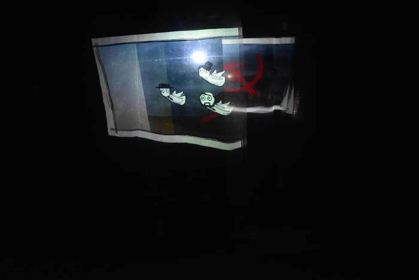 Hand-drawn animation projected on stage, showing three floating figures beside a hammer-and-sickle symbol.