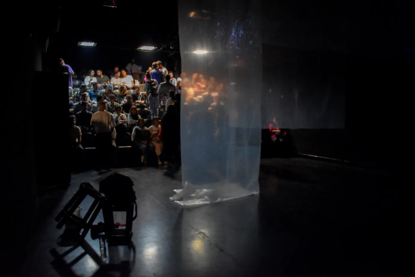 The audience and stage seen together, with a lit fabric screen dividing the space.